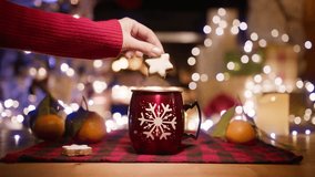 Female hand in red sweater soak in hot tea star shape gingerbread cookie on blurred christmas tree light and burning fire background. Cozy Christmas eve in festive decorated living room with fireplace - Powered by Shutterstock - Get 15% off with code: PIKWIZARD15