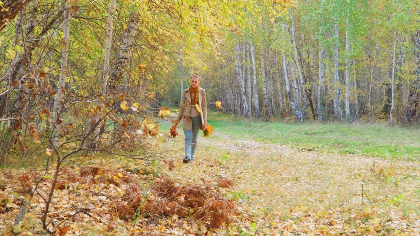 A red-haired girl walks through the autumn forest, enjoying the autumn nature. In her hands she holds a bouquet of autumn leaves.