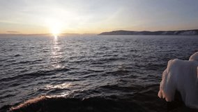 Video of Baikal Lake at sunset in December. Waves crash against an icy pier against the backdrop of the setting sun. Beautiful seascape. Natural background. Travels along the lake shore