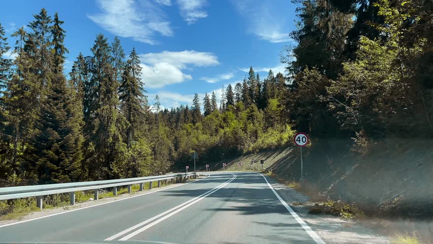 Driving on asphalt road among forest in mountains. Mountain trip by car among beautiful landscape.