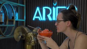 This video shows a side view of a woman sipping a fancy strawberry cocktail at a bar.