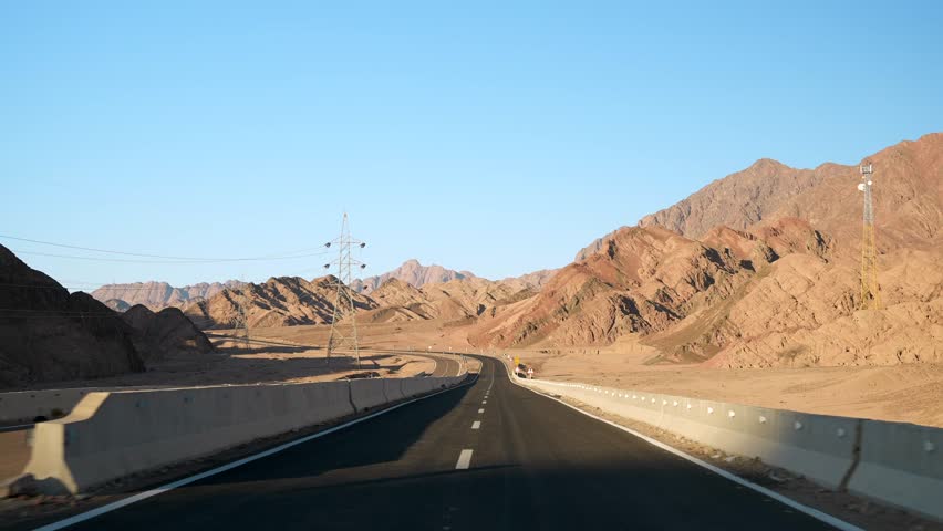 Front view of car driving on the empty asphalt highway in the desert with road surface marking lines. Sand mountains on the roadside and the hot sun in the blue sky