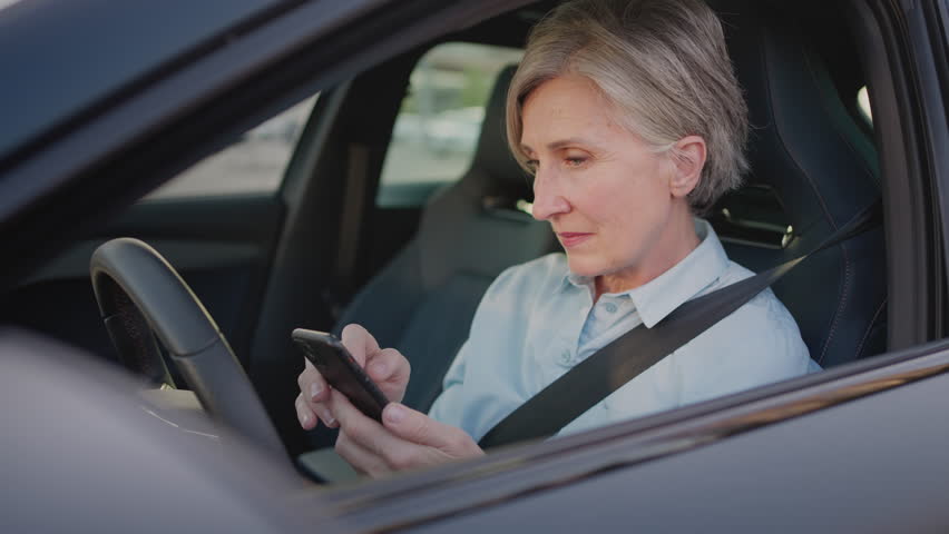 Elderly woman sitting in modern auto fastened with seat belt and receiving terrible news on smartphone. Stressed woman in casual clothes feeling dizziness and desperately touching forehead. Royalty-Free Stock Footage #1109267779