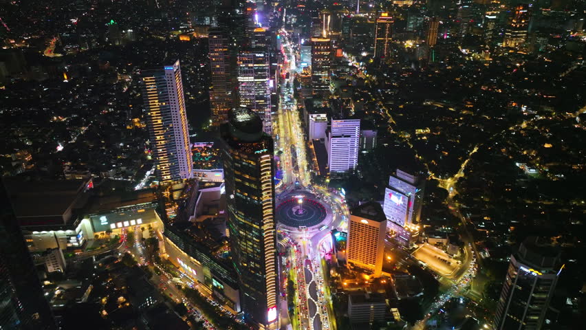 Aerial View of traffic on roundabout around Selamat Datang monument, Multi lane highway in large urban city center Cityscape of high rise buildings in Jakarta, Indonesia at night Royalty-Free Stock Footage #1109269991