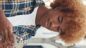 Vertical video, Guy with an African hairstyle wearing blue shirt uses mobile phone outside on the street - Powered by Shutterstock - Get 15% off with code: PIKWIZARD15