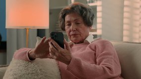 Caucasian old lady grandmother senior woman mature retired female using modern tech smartphone serious at evening home reading news scrolling mobile phone internet service at sofa shopping online app - Powered by Shutterstock - Get 15% off with code: PIKWIZARD15