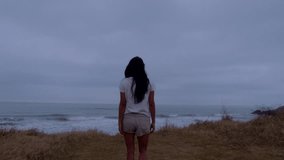 4k video of a girl wearing shorts moving towards the waves of the sea