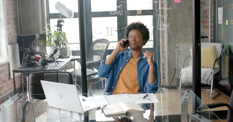 African american casual businessman sitting at desk talking on smartphone at home, slow motion. Communication, home office, remote working and casual business, unaltered. | Shutterstock HD Video #1109275525