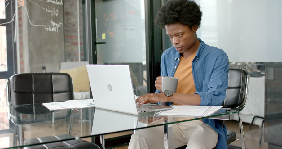 African american casual businessman using laptop and drinking coffee at desk, slow motion. Communication, home office, remote working and casual business, unaltered. | Shutterstock HD Video #1109275587