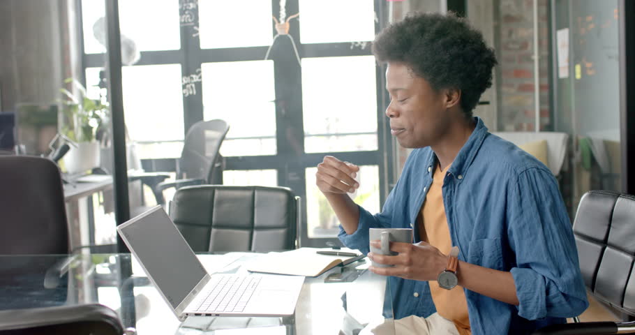 Happy african american casual businessman at desk having laptop video call and coffee, slow motion. Communication, home office, remote working and casual business, unaltered. | Shutterstock HD Video #1109275893