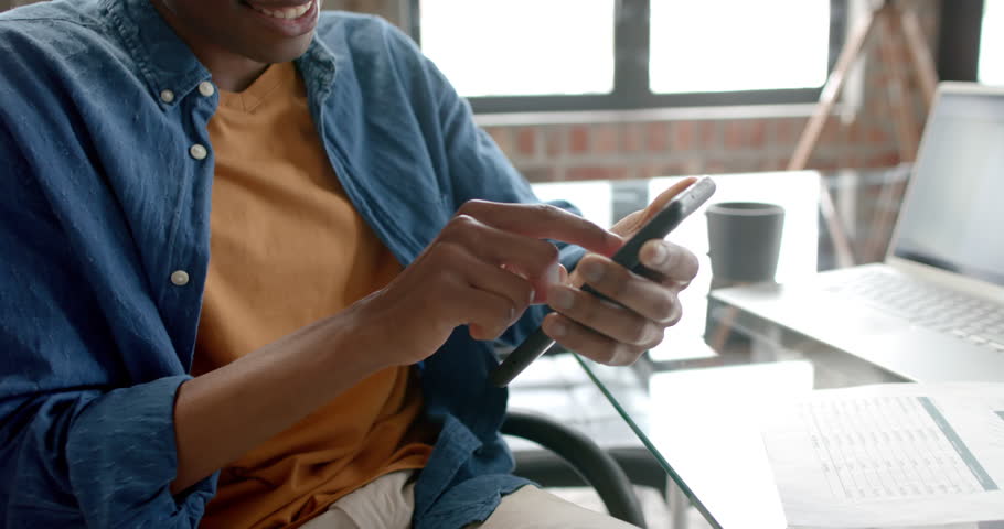 Midsection of african american casual businessman sitting using smartphone at home, slow motion. Communication, home office, remote working and casual business, unaltered. | Shutterstock HD Video #1109276237