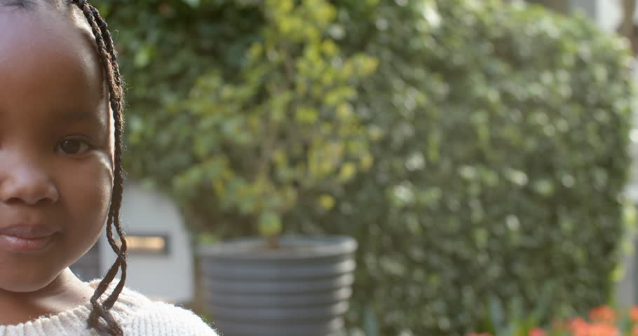Portrait of african american girl with braided hair smiling in sunny garden, copy space, slow motion. Childhood, free time, wellbeing and lifestyle, unaltered. | Shutterstock HD Video #1109276475