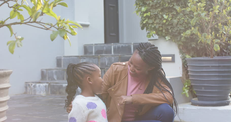 Happy african american mother and daughter sitting and talking in garden, slow motion. Motherhood, childhood, togetherness, family and lifestyle, unaltered.