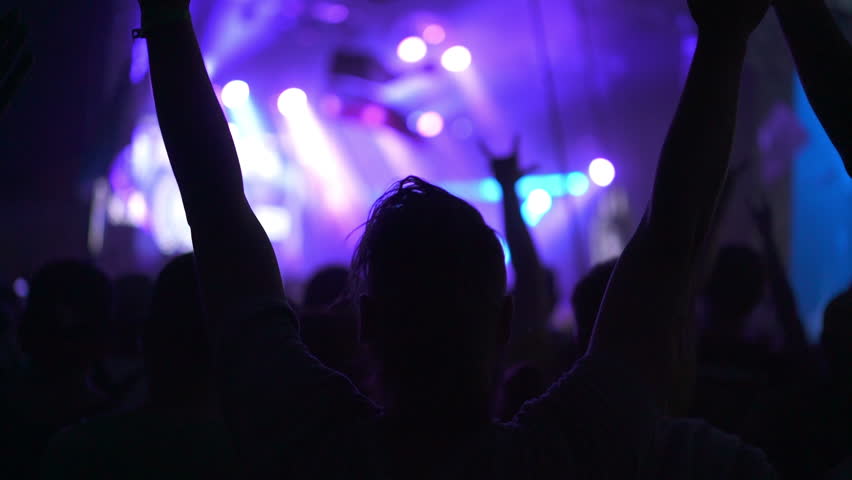 Rock Band with Guitarists and Drummer Performing at a Concert in a Night Club. Front Row Crowd is Partying. Silhouettes of Fans Raise and clap Hands in Front of Bright Colorful Strobing Light on Stage Royalty-Free Stock Footage #1109279081