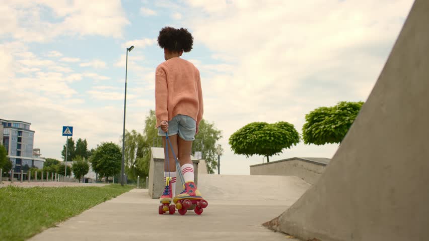 A girl plays by pulling roller skates by the laces behind her.