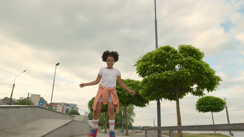 Cute African American little girl riding on roller skate in summer park. Kid enjoying outdoor sport in the park, Funny little girl playing on roller skate on road. sport learning outdoor concept