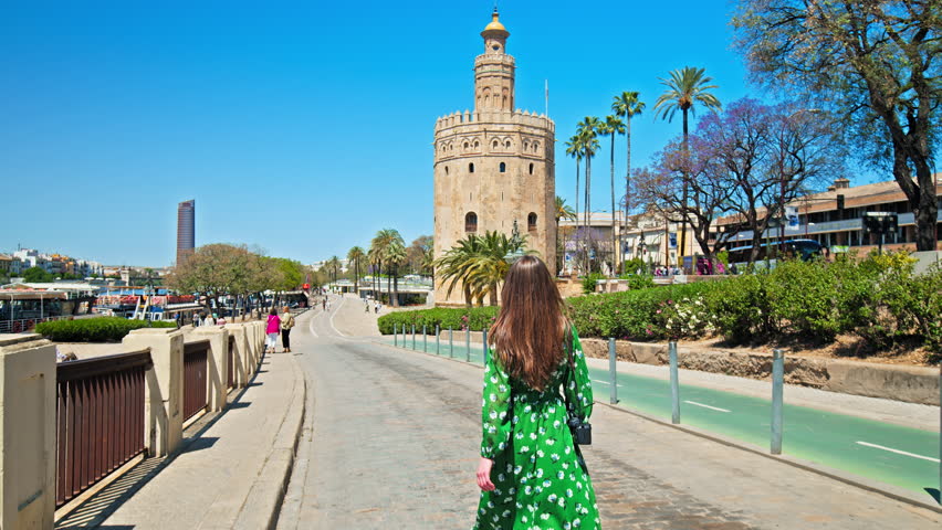 Tourist girl in a dress walking towards Torre del Oro Fortress in Seville, Spain. A female woman looking at the Spanish Old defensive military watchtower in Seville, Europe