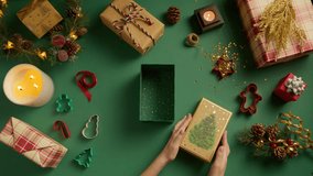 Overhead female hands opening green and golden gift box with christmas tree drawing on green background. Presents wrapped in kraft paper for new year celebration. Holiday shopping background top view - Powered by Shutterstock - Get 15% off with code: PIKWIZARD15