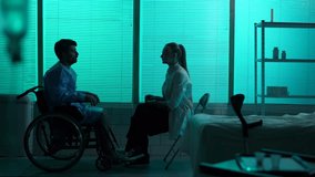 Full-sized silhouette video a disabled man, patient with mobility impairment on a wheelchair talking to a female doctor who tells him bad news. The man is shocked and desperate.