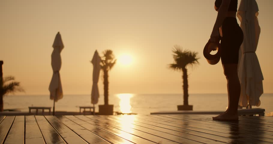 Close-up shot of a girl in a black sports summer uniform spreading a mattress for yoga against of a golden sunset on the beach. Yoga and meditation classes in the evening on Sunny Beach Royalty-Free Stock Footage #1109292347