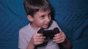 child a boy of six years old is sitting on the couch at home in the evening and playing video games with a black joystick - Powered by Shutterstock - Get 15% off with code: PIKWIZARD15