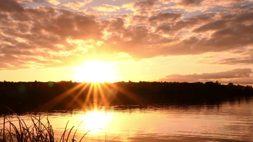 Shining sun with its rays above a lake. sunset on the horizon in front of the water. Very cloudy sky.
