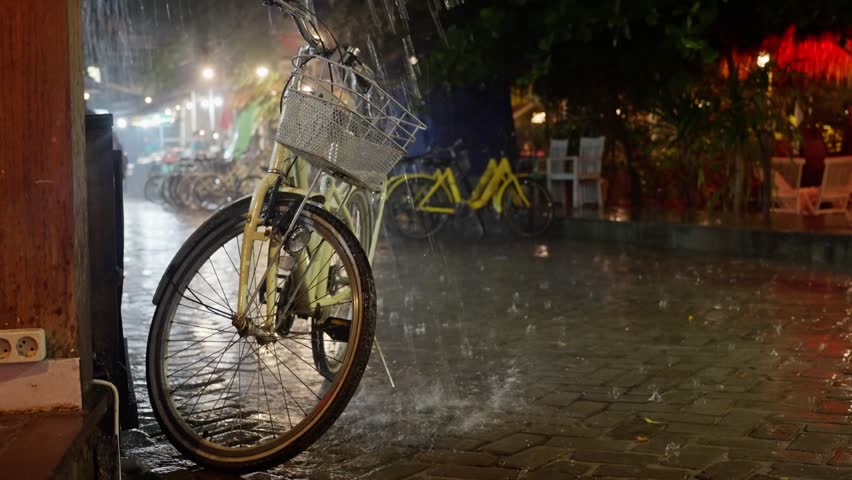 Heavy downpour in the bicycle parking at night, Retro yellow bicycle with bicycle bag, gets wet in the rain at night. yellow Bicycle stands in the rain on the street, close-up Royalty-Free Stock Footage #1109302357