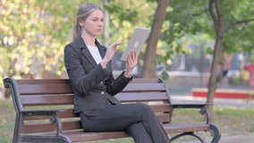 Businesswoman Doing Video Chat on Tablet while Sitting Outdoor on a Bench