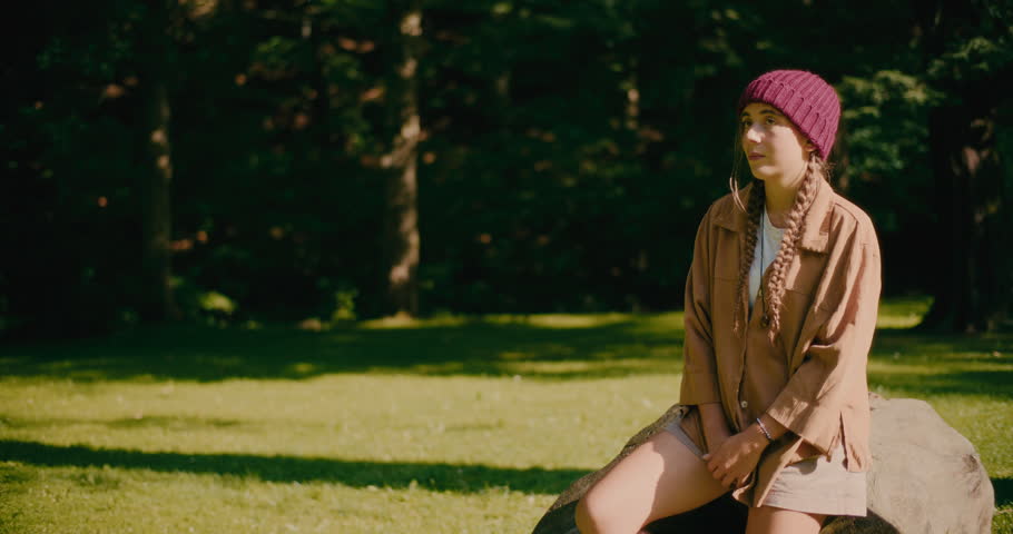 Sad young woman sitting on rock at park during sunny day