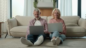 Successful happy mature caucasian married couple man woman entrepreneurs grandfather grandmother using laptops computer remote work on Internet together communicate on social network in living room - Powered by Shutterstock - Get 15% off with code: PIKWIZARD15