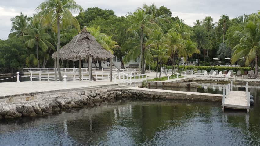 View of hotel resort pier with cabana and palm trees along ocean front in Key Largo, Floriday Keys beach landscape - 4K Drone