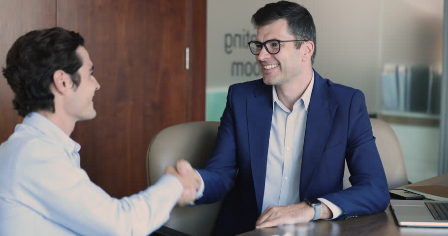 Smiling middle-aged businessman in suit and client handshake, closing successful deal, seated at desk in modern office meeting room, satisfied employer, manager hiring new employee. HR, make business | Shutterstock HD Video #1109316749