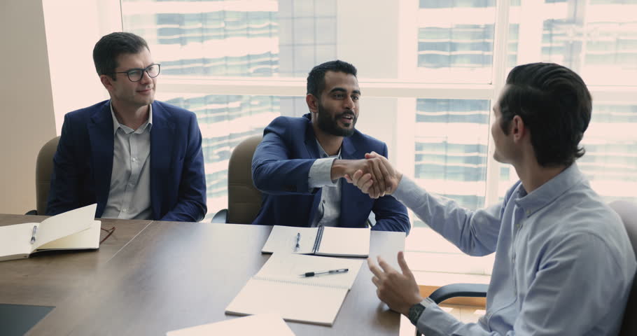 Three multi-ethnic businessmen negotiate together in boardroom, make profitable commercial deal, shake hands express respect after effective formal meeting. Trust, legal commitment, business etiquette | Shutterstock HD Video #1109316773