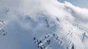 Ski hill on sunny winter day with scenic cloud. Skiers and snowboarders skiing on snow slopes with ski lift. Aerial drone footage of skiers and snowboarders on Mammoth lakes resort with snowy mountain
