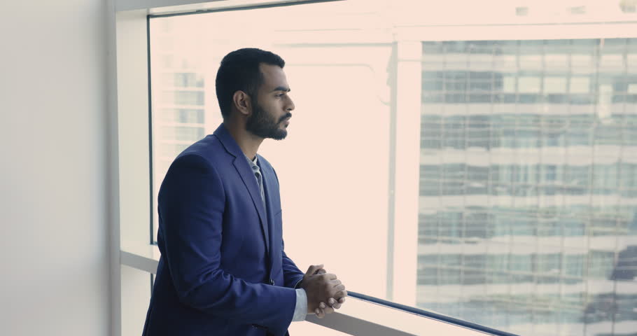 Young thoughtful Indian businessman in suit stand in modern skyscraper office, look out window, thinks of future, deep in thoughts about start up ideas, goals or project. Business vision, aspirations Royalty-Free Stock Footage #1109318361
