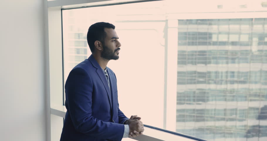 Young thoughtful Indian businessman in suit stand in modern skyscraper office, look out window, thinks of future, deep in thoughts about start up ideas, goals or project. Business vision, aspirations | Shutterstock HD Video #1109318361