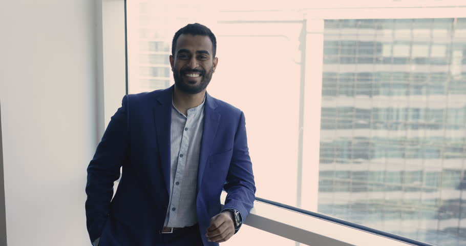 Millennial happy Indian businessman in formal suit posing near window smile look at camera enjoy break, standing indoor. Portrait of successful, promoted office employee, company CEO, executive, boss | Shutterstock HD Video #1109318367