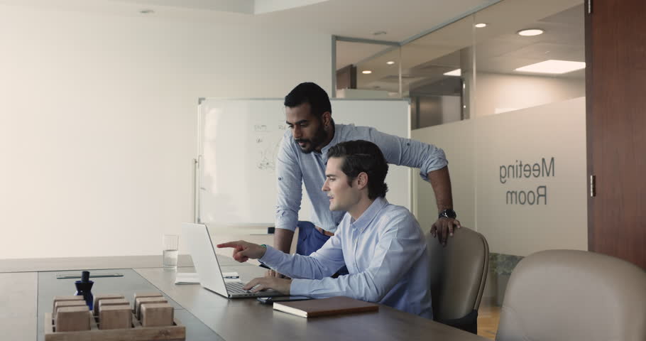 Indian and Hispanic associates using laptop in meeting room, reviewing new app, develop marketing strategy, working on start-up ideas. Mentor helps to colleague with software, share skills. Teamwork | Shutterstock HD Video #1109318391