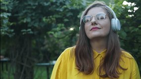 Slow motion of happy Caucasian 30s woman in headphones and glasses dancing singing outdoors in city street having fun alone. High quality FullHD footage