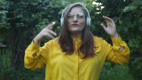 Slow motion of happy Caucasian 30s woman in headphones and glasses dancing singing outdoors in city street having fun alone. High quality FullHD footage