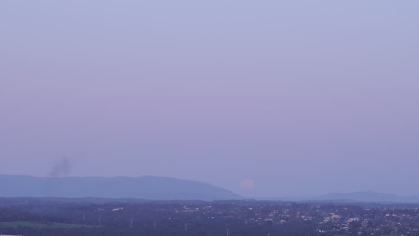 Time lapse at dusk of a purple sunset, the full Moon in an bright orange color rising over a mountain