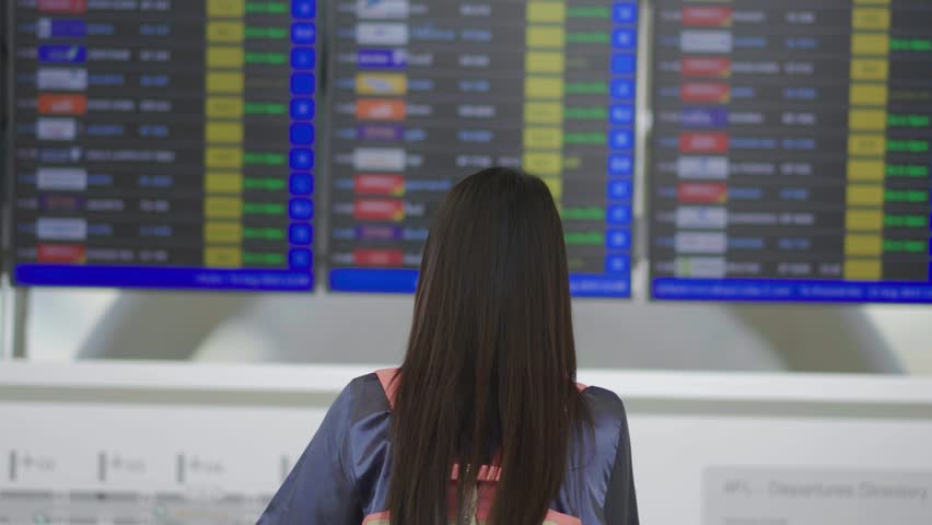 Young asian woman with passport and boarding pass as a hand stand in front of the airline time schedule board looking at the flight information board at the airport terminal, checking her flight Royalty-Free Stock Footage #1109323515