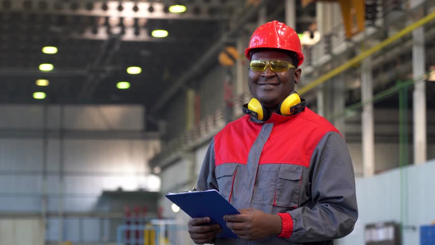 Smiling Industrial African American Worker in Personal Protective Equipment Giving Thumb Up. Portrait Of Black Industrial Worker In Red Helmet, Yellow Safety Goggles And Work Uniform In A Factory. Royalty-Free Stock Footage #1109324355