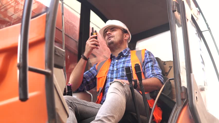 Young man loader worker or a forklift driver in a container warehouse wearing a white helmet is talking on the walkie-talkie or radio phone while sitting in the car. Royalty-Free Stock Footage #1109327663