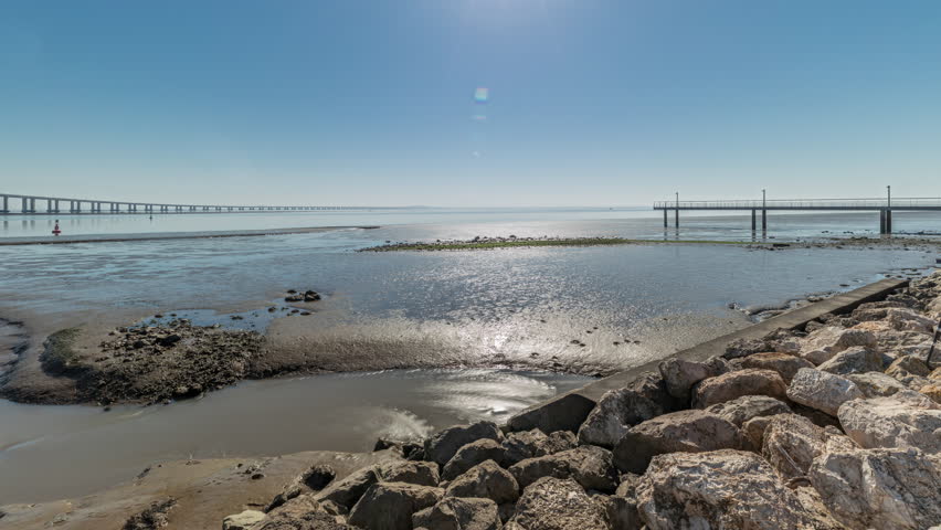 Panorama showing motion from the low to high tide next to Vasco da Gama Bridge in Parque das Nacoes timelapse in Lisbon, Portugal. Level of water is rising up. Waterfront in Park of Nations district