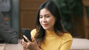 happy smiling asian young woman in yellow sweater sitting on sofa and having video call on smartphone at home