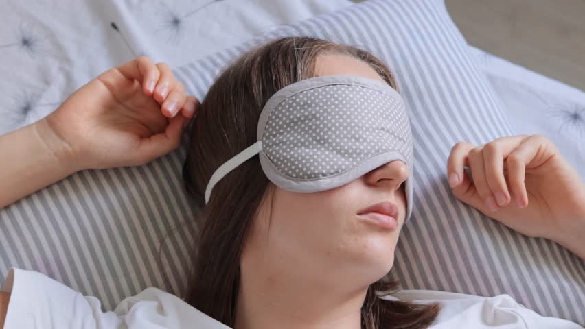Calm brown haired girl in bed wearing sleep mask for complete darkness, peace and quiet all night long, woman on pillow in the bedroom having day nap. Royalty-Free Stock Footage #1109333965