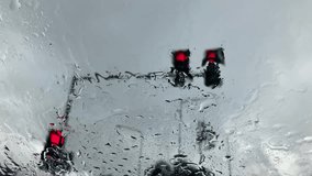Raindrops flow down the glass on the car window with a blurred background of the red traffic light in the morning. Bokeh. Close up. It rains in the rainy season.