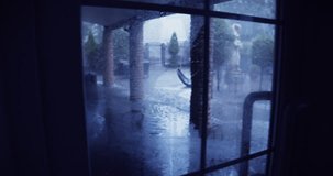Tilt view of a cozy garden that has been hit by heavy rain. A summer hurricane in Latvia knocked down furniture and trees. Raindrops splash. The rain hits large puddles on the paving stones. 4K video