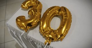 Half panorama and zoom in gold Helium Balloon with Number 30 thirty years birthday anniversary golden balloon. The balls lie on a white tablecloth on the table. Birthday, anniversary, date concept. 4K